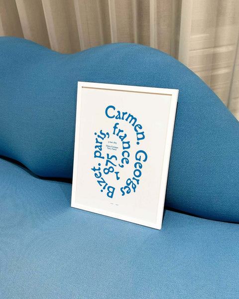 Carmen art print with bold blue typography in white frame on blue sofa